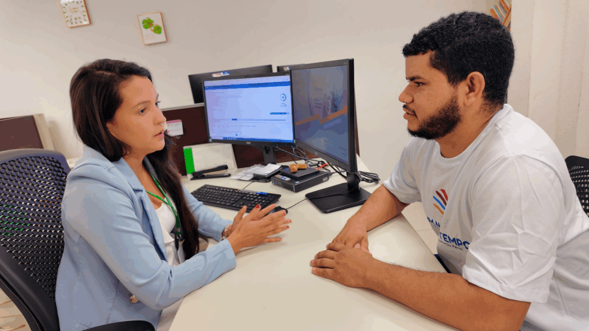 Um homem e uma mulher conversando, sentadas, em uma mesa no local de trabalho