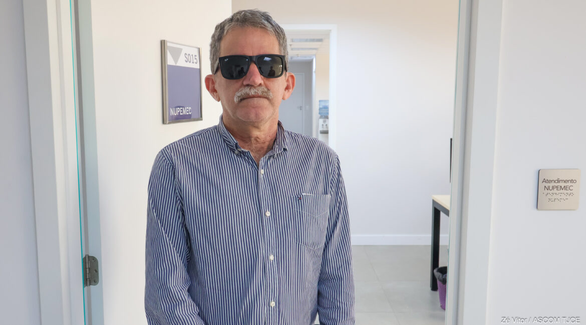 Foto de um homem, usando óculos escuros, na sala do Nupemec