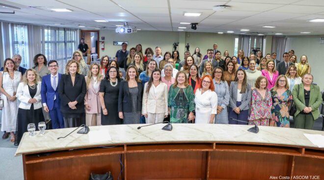 Dezenas de pessoas enfileiradas e em pé sorriem dentro de um auditório Dezenas de pessoas enfileiradas e em pé sorriem dentro de um auditório
