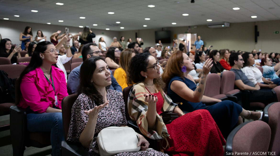 Várias mulheres sentadas no auditório, cantando e movimentando as mãos
