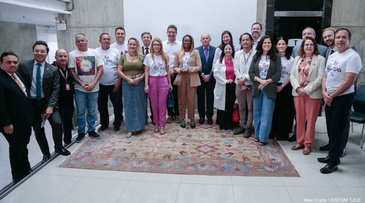 Foto com várias pessoas, em pé, sorrindo, em uma grande sala