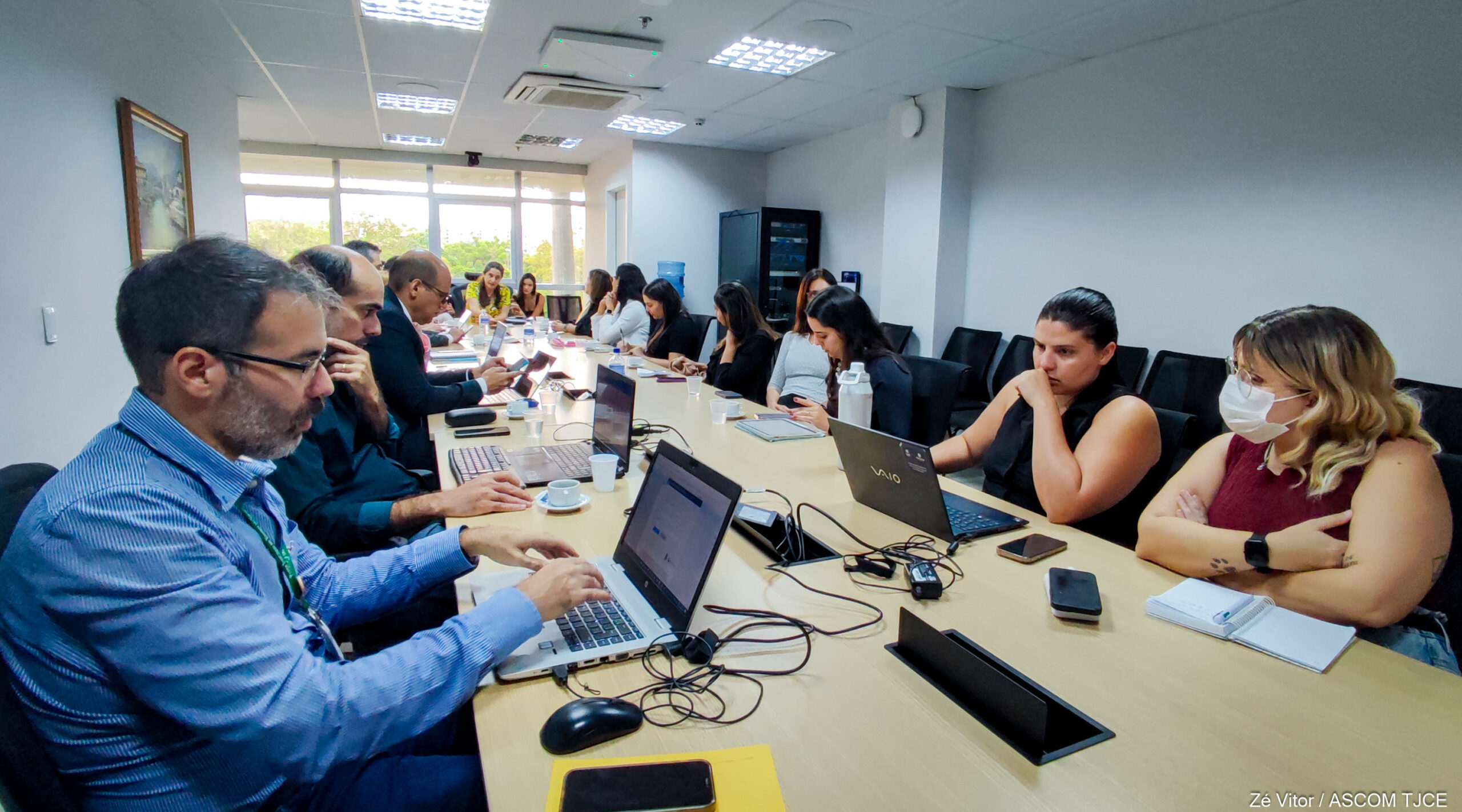 Foto de várias pessoas sentadas em uma grande mesa redonda de trabalho