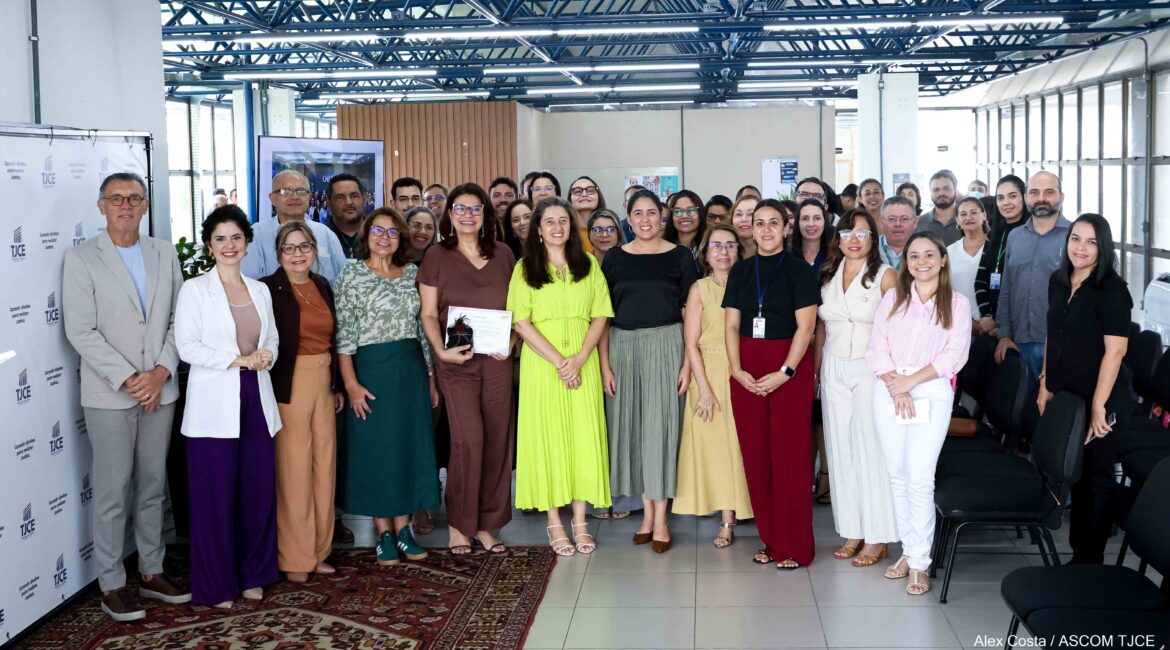Foto com várias mulheres e homens, em pé, sorrindo, em um espaço amplo