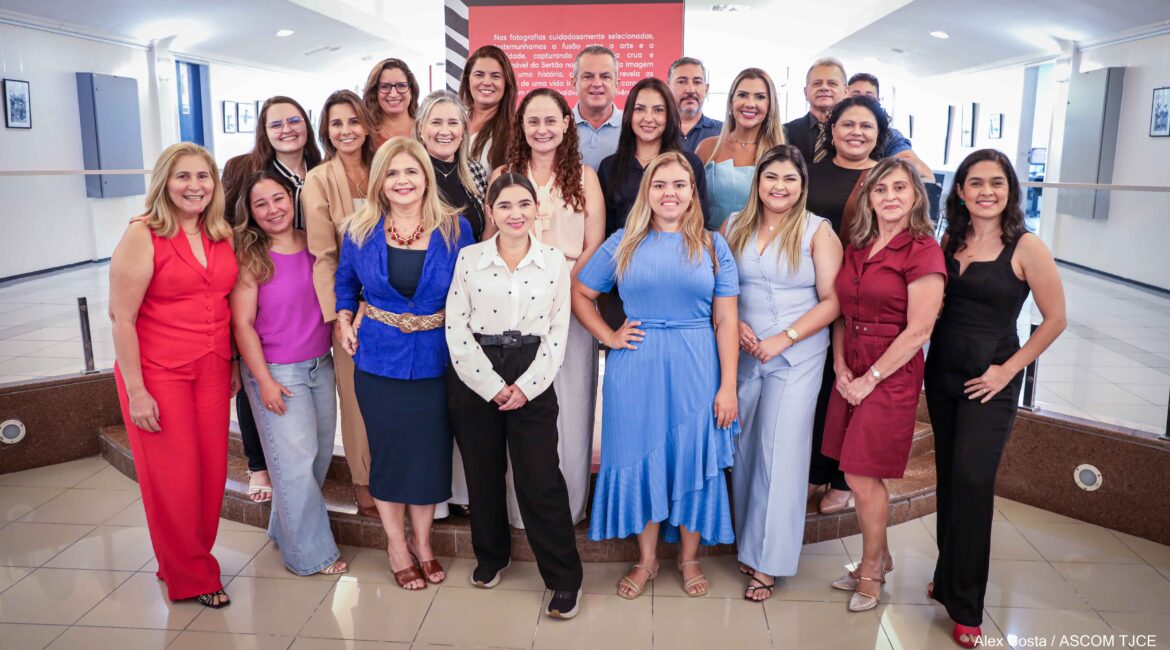 Foto com várias mulheres, uma ao lado da outra, sorrindo, no hall da Escola