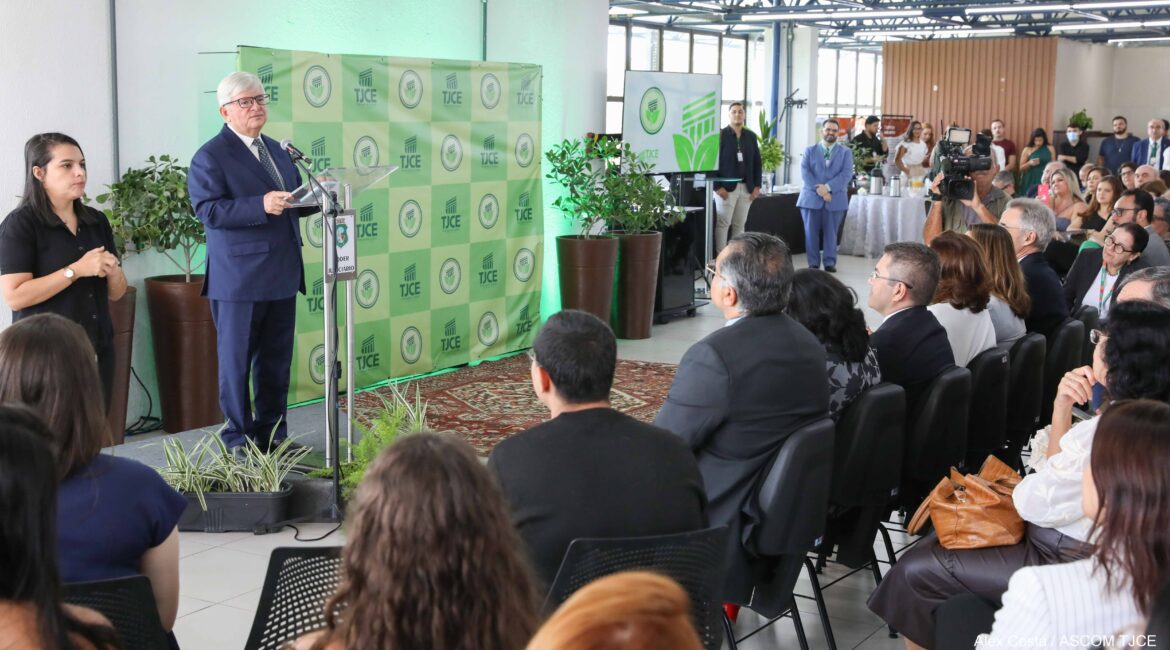 Foto de um homem falando ao microfone e, à frente dele, várias pessoas sentadas na plateia Foto de um homem falando ao microfone e, à frente dele, várias pessoas sentadas na plateia