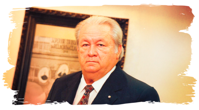 Foto do um homem branco, sério, cabelos brancos e de paletó, em uma arte de cor dourada 