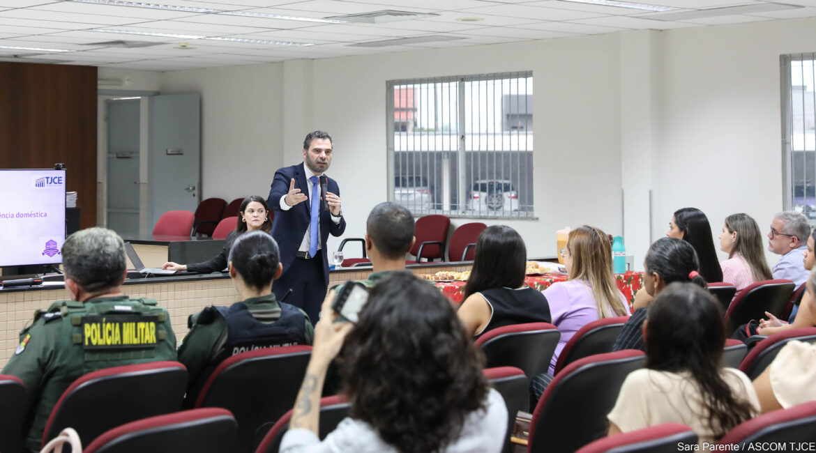 Foto de um homem falando ao microfone e, na frente dele, várias pessoas na plateia, sentadas
