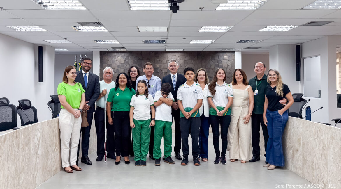 Imagem com várias mulheres, homens e crianças posando para foto em pé, sorrindo, num grande auditório