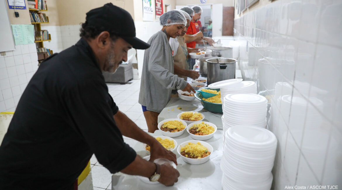 Foto de hmens e mulheres efileiradas(os) colocando comida nas quentinhas