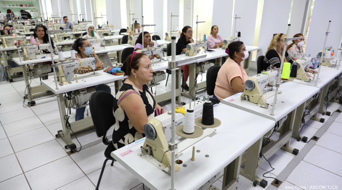 Foto com várias mulheres sentadas em mesas, aprendendo a costurar em máquinas Foto com várias mulheres sentadas em mesas, aprendendo a costurar em máquinas