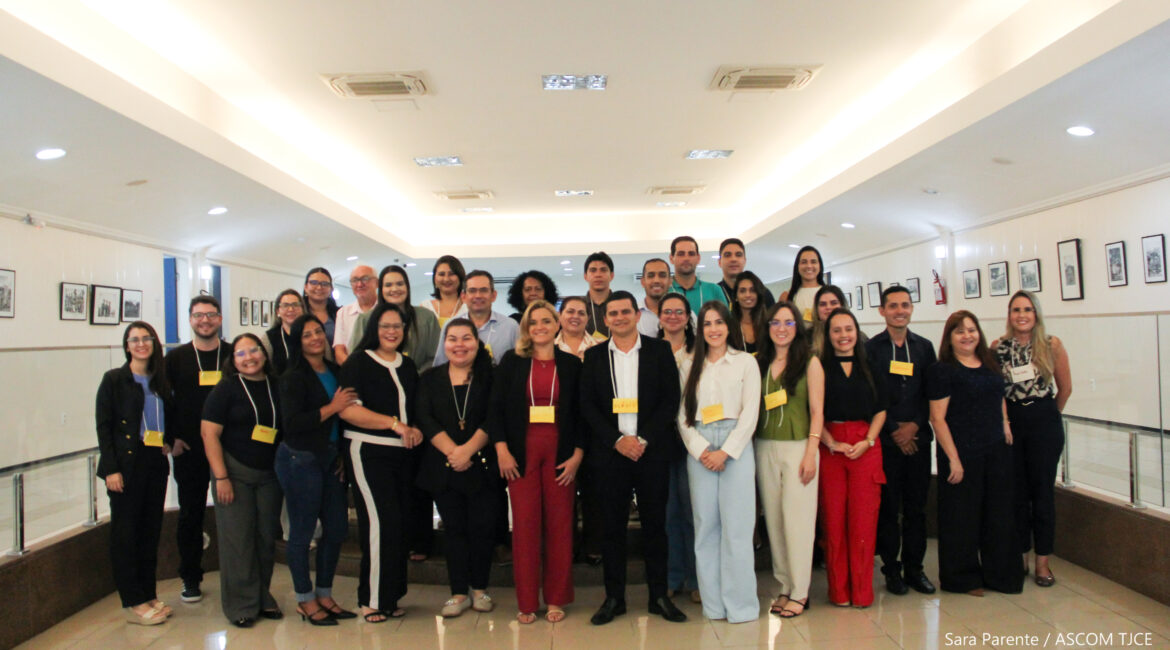Imagem com vários homens e mulheres, sorrindo, posando para fato, no hall da Esmec