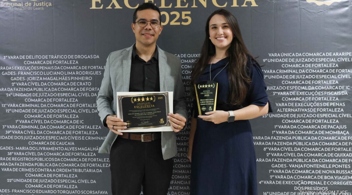 Imagem de uma mulher e um homem posando para foto, sorrindo e exibindo a premiação
