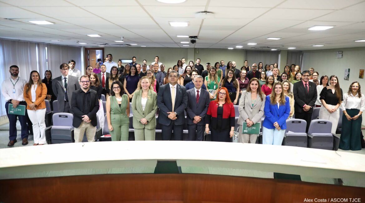 Imagem de várias mulheres e homens, posando em pé para foto, sorrindo em um grande auditório