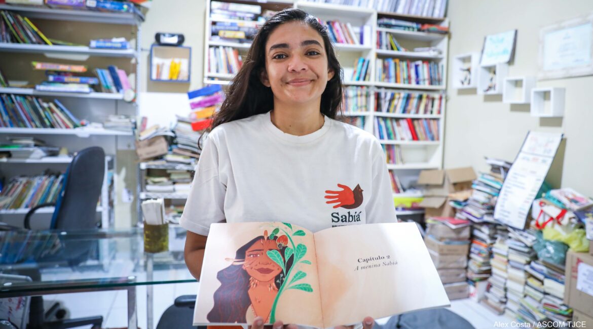 Foto de uma mulher sorrindo, segurando um livro aberto