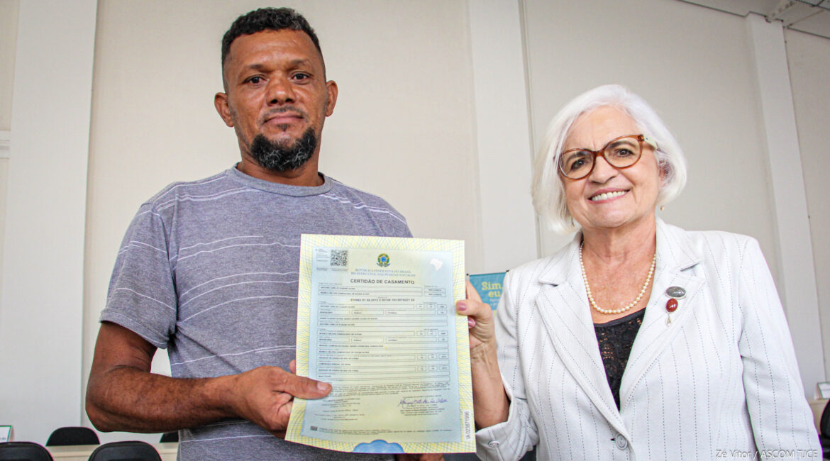 Foto de um homem e uma mulher, sorrindo, e ambos exibindo a certidão de nascimento