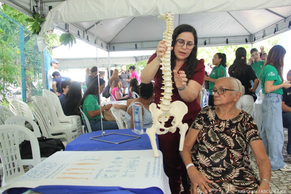 Foto de uma mulher em pé, explicando o funcionamento da coluna vertebral para uma senhora idosa que está sentada