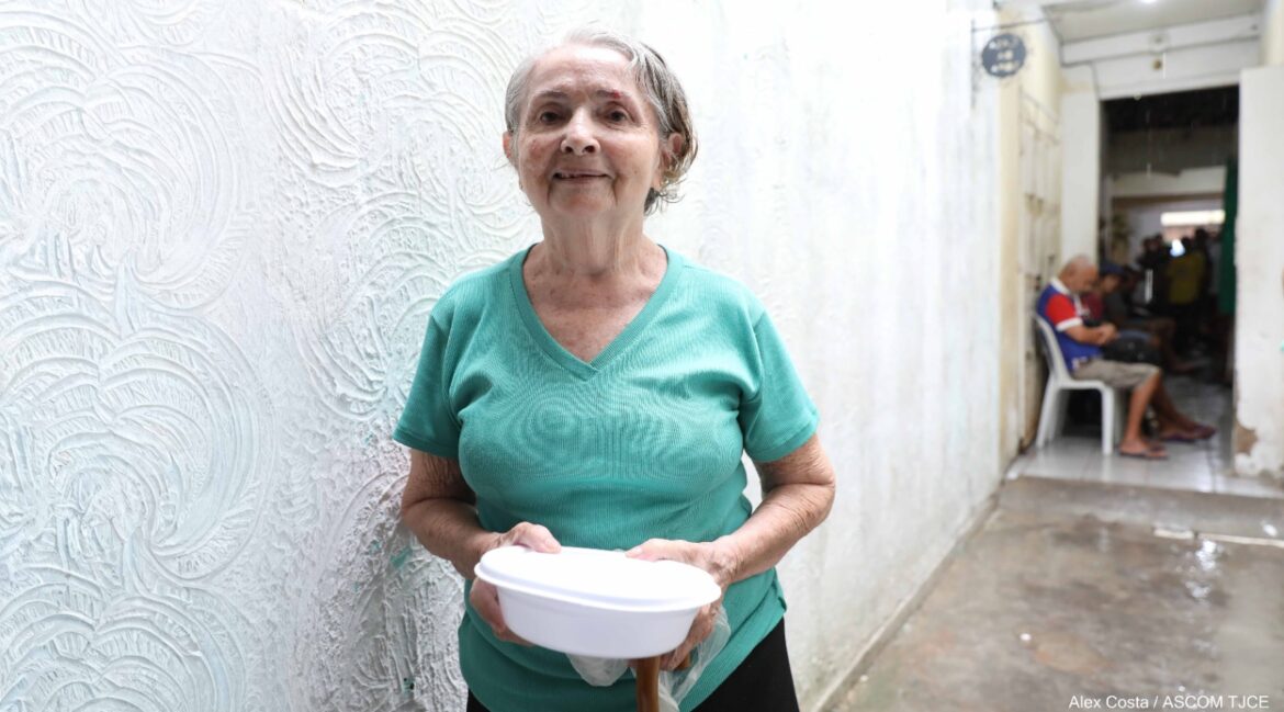 Foto de uma senhora idosa, sorrindo com uma quentinha na mão