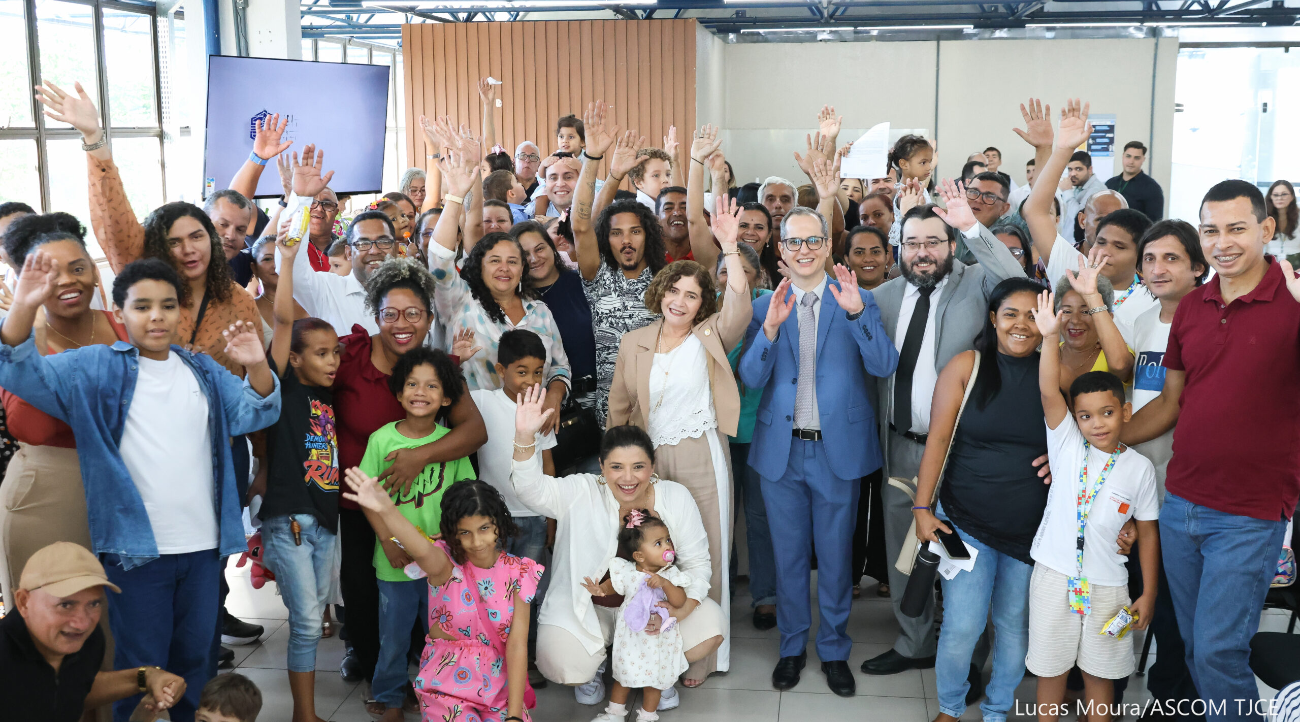 Grupo de famílias e profissionais de adoção reunidos sorrindo, comemorando a entrega e o recebimento dos documentos.