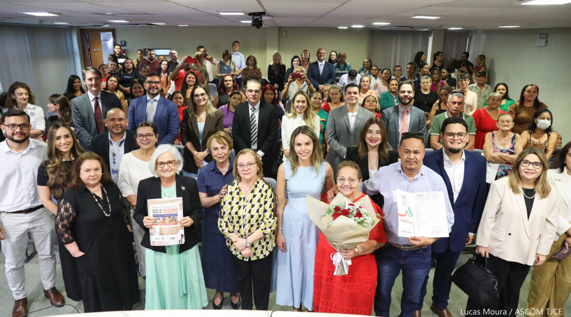 Várias pessoas posando para foto, em pé, sorrindo em um grande auditório