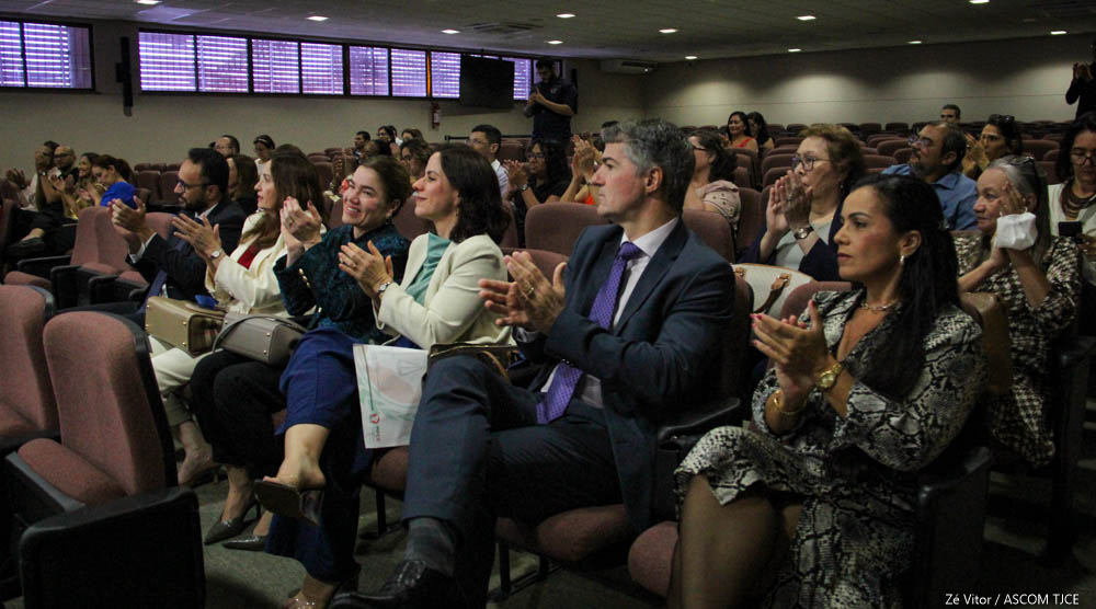 Várias pessoas sentadas no auditório aplaudindo e sorrindo Várias pessoas sentadas no auditório aplaudindo e sorrindo