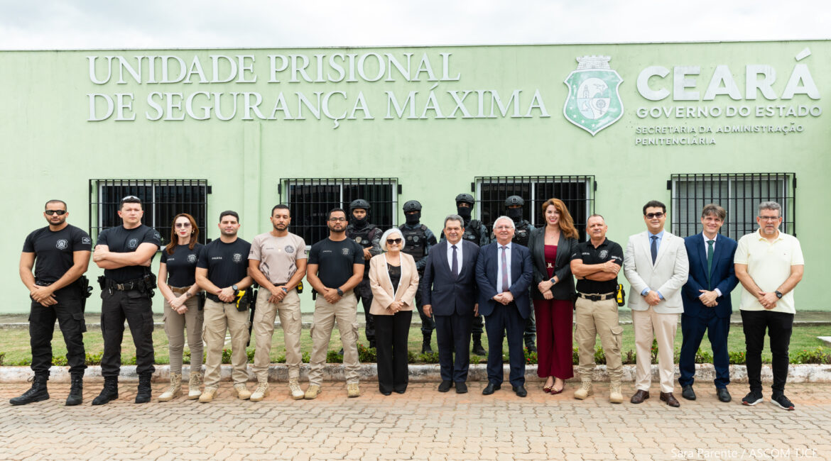 Imagem com vários homens e mulheres posando para foto. Ao fundo da imagem, uma parede na cor verde claro, com inscrições: Unidade Prisional de Segurança Máxima e Ceará-Governo do Estado Imagem com vários homens e mulheres posando para foto. Ao fundo da imagem, uma parede na cor verde claro, com inscrições: Unidade Prisional de Segurança Máxima e Ceará-Governo do Estado