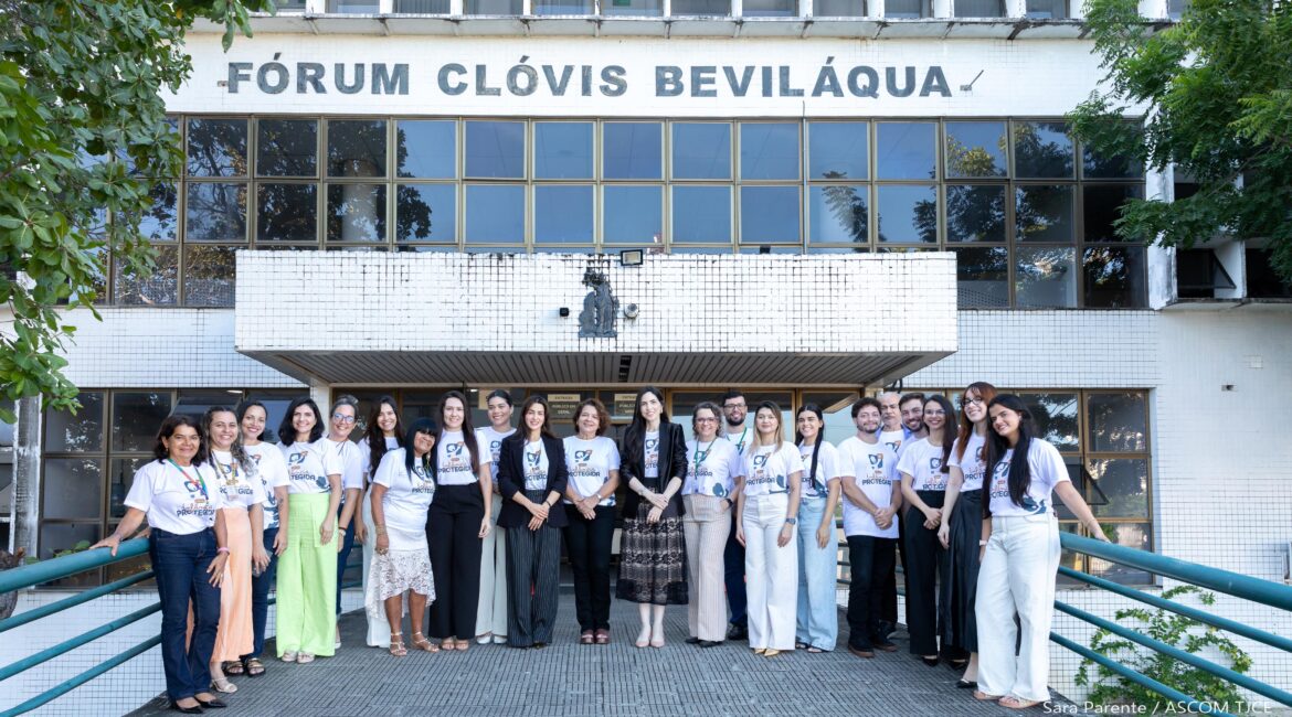 Imagem de mulheres e homens posando para foto, sorrindo e, ao fundo, a fachada do Fórum Clovis Beviláqua Imagem de mulheres e homens posando para foto, sorrindo e, ao fundo, a fachada do Fórum Clovis Beviláqua