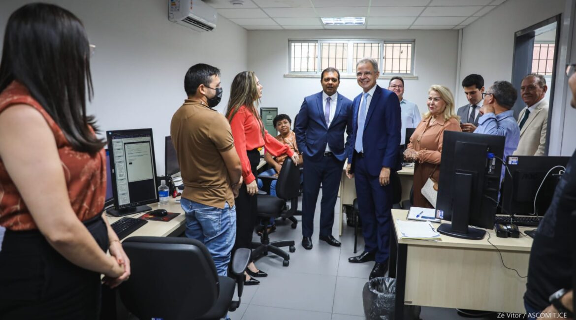 Em uma sala com mesas e computadores, várias pessoas em pé, descontraídas, sorrindo Em uma sala com mesas e computadores, várias pessoas em pé, descontraídas, sorrindo