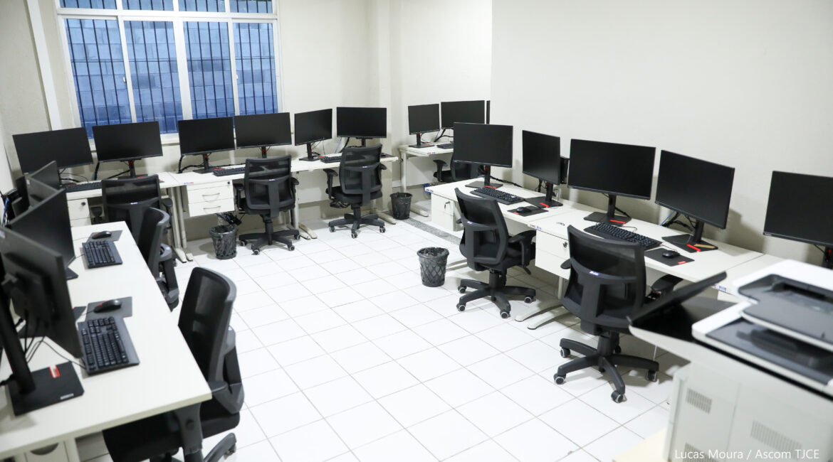 Foto de uma sala com bancadas de trabalho e vários computadores