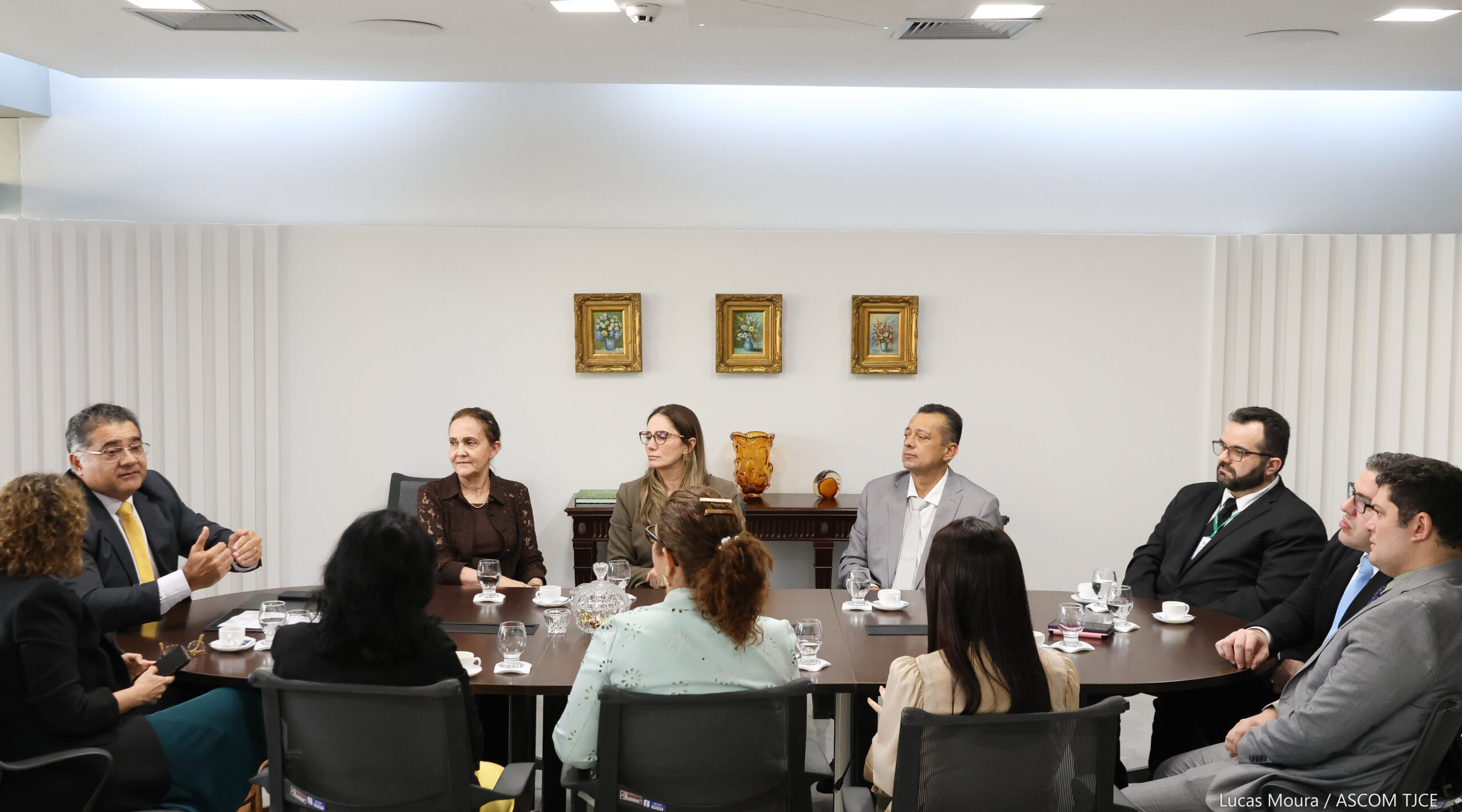 Foto com vários homens e mulheres sentados em uma mesa de trabalho, dialogando