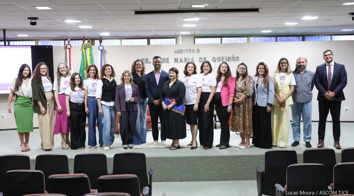 Imagem de 18 pessoas posando para foto, sorrindo, em pé, no palco do auditório Imagem de 18 pessoas posando para foto, sorrindo, em pé, no palco do auditório