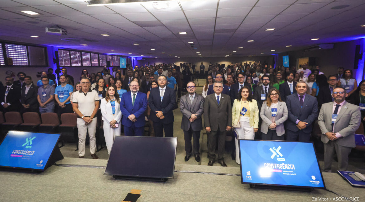 Imagem de várias pessoas posando para foto, em pé, em um grande auditório