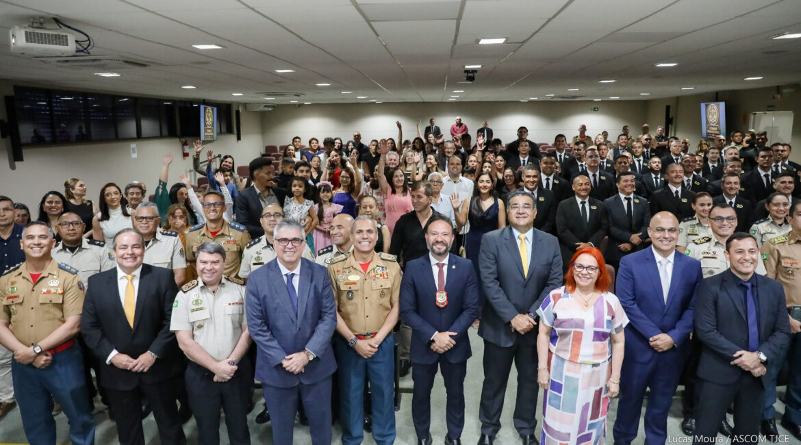 Imagem de várias pessoas em pé, posando para foto, sorrindo, em um grande auditório