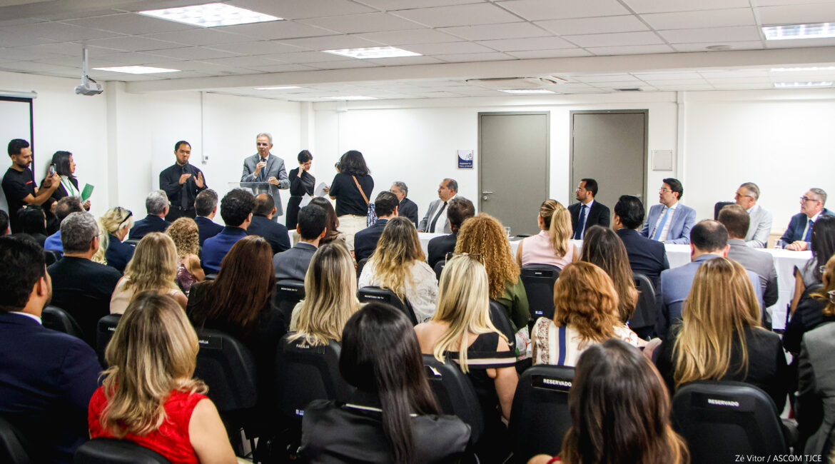 Foto de auditório lotado de pessoas, sentadas, e, em pé, um homem falando ao microfone