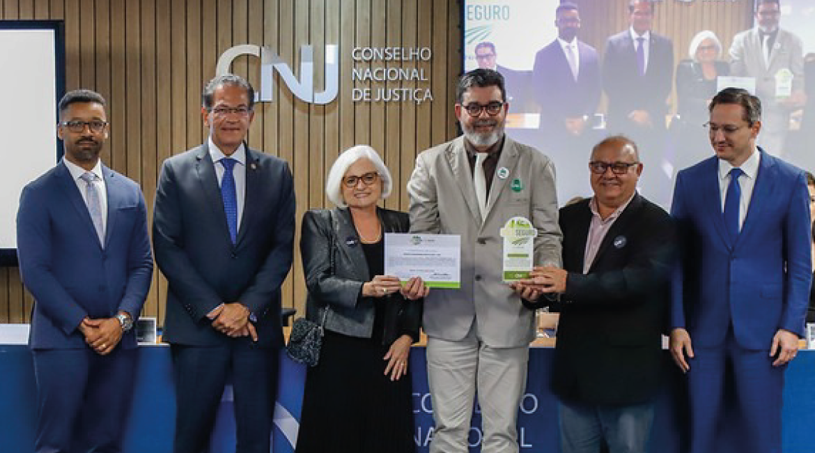 Foto de cinco homens e uma mulher posando para foto, sorrindo, e exibindo certificado e placa de reconhecimento