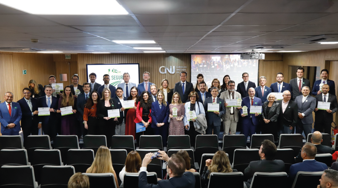 Imagem de várias mulheres e homens posando para foto, sorrindo, em um amplo auditório Imagem de várias mulheres e homens posando para foto, sorrindo, em um amplo auditório