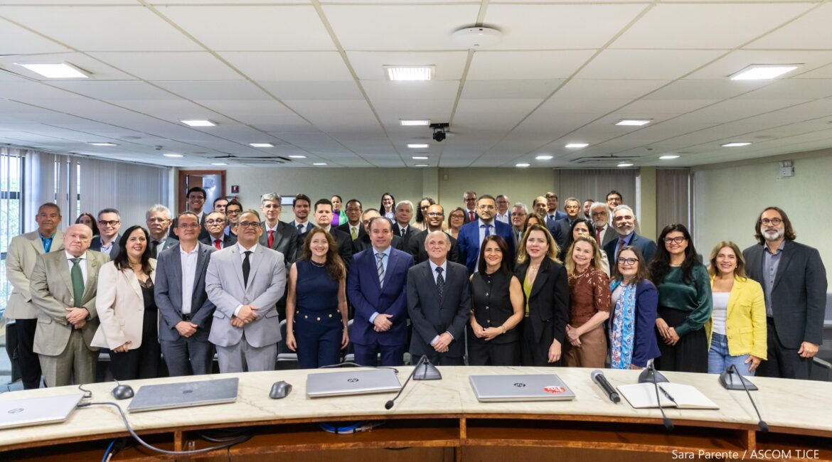 Imagem de várias mulheres e homens posando para foto, em pé, em um auditório