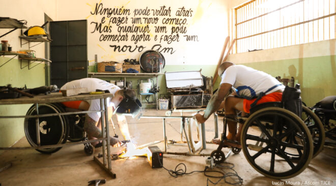 Dois homens em cadeiras de rodas fazem reparos com soldas em estruturas de metal