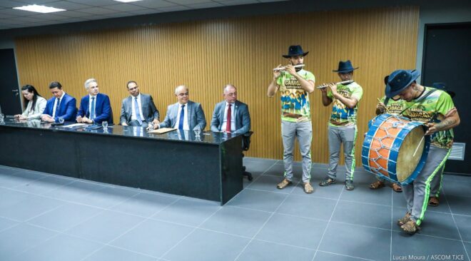 Grupo musical com roupas coloridas se apresenta. Ao lado, representantes do Judiciário assistem
