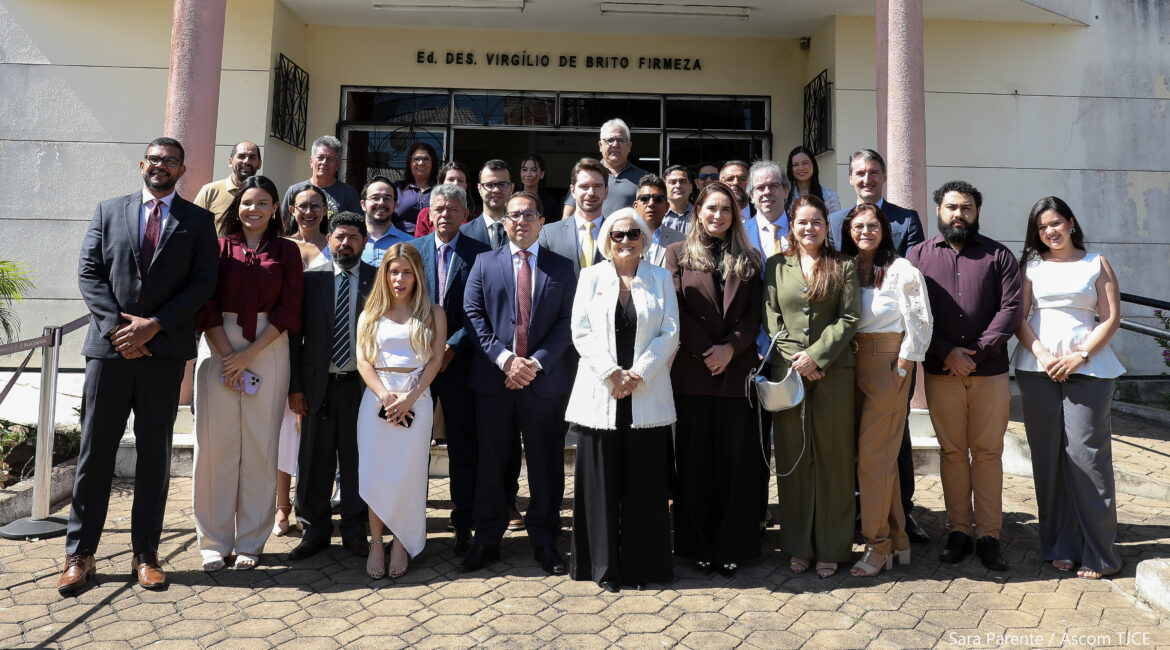 Foto de várias pessoas em pé, posando para foto, sorrindo, na frente da fachada do Fórum