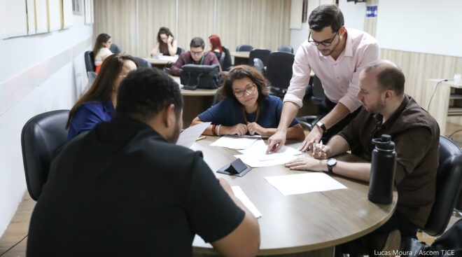 Foto de homem ensinando alunos em torno de uma mesa redonda.