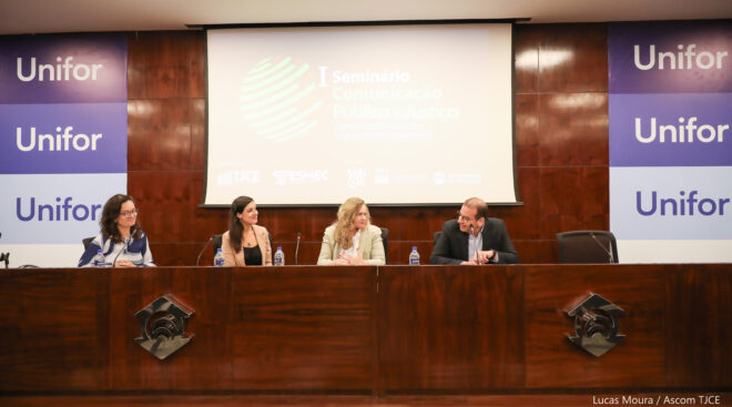 Foto de 3 mulheres e um homem em uma mesa de debates no palco de auditório