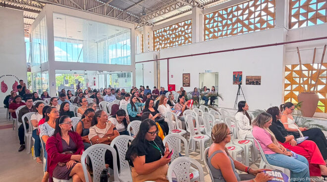 Fotografia de diversas pessoas sentadas em cadeias de plástico, formando uma plateia.