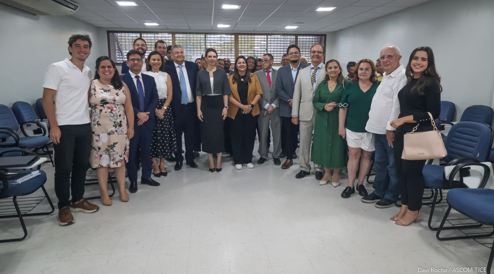 Imagem de homens e mulheres sorrindo para foto, em pé, em uma sala