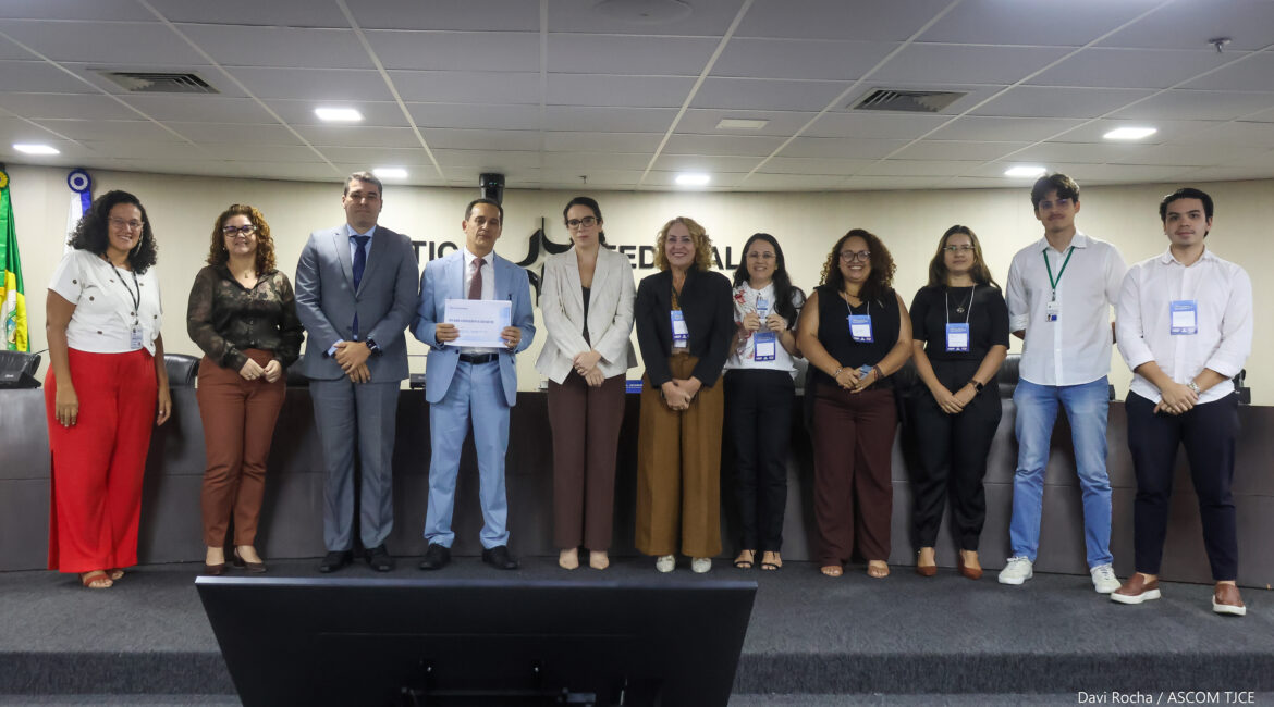 Imagm de vários homens e mulheres perfilhados, posando para foto em pé e sorrindo no auditório
