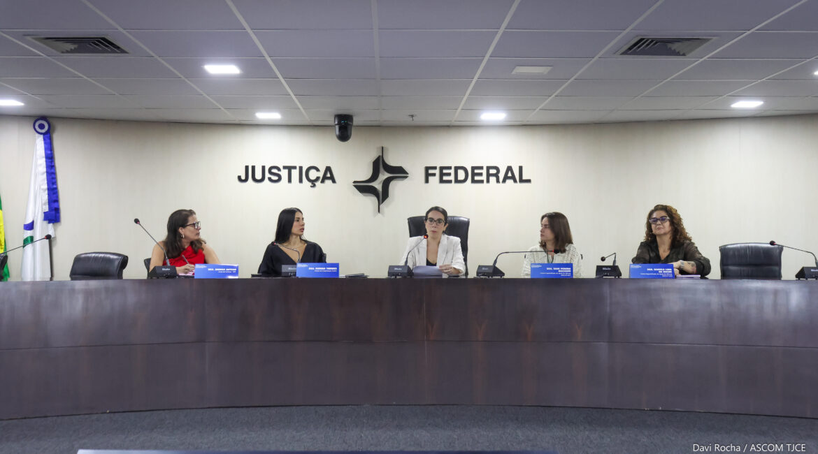 Foto de uma grande mesa, no palco, em que se encontram cinco mulheres debatendo as temáticas