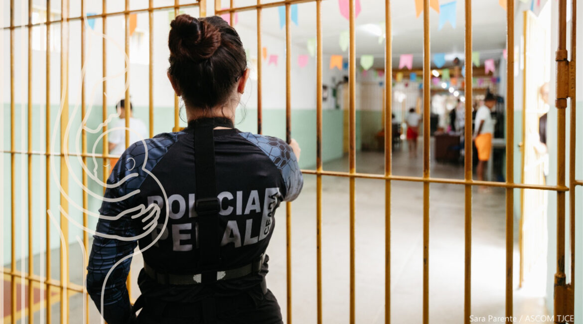 Foto de uma policial obervando mulheres presas, entre uma grade de ferro que as separa