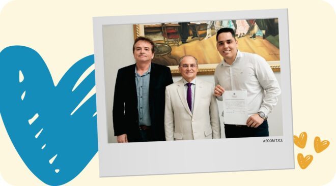 Foto colorida inserida como um post it, em um fundo amarelo bem claro, com um coração azul maior no lado esquerdo e pequenos corações amarelos escuros no canto inferior direito. Na fotos, três homens posam sorridentes.
