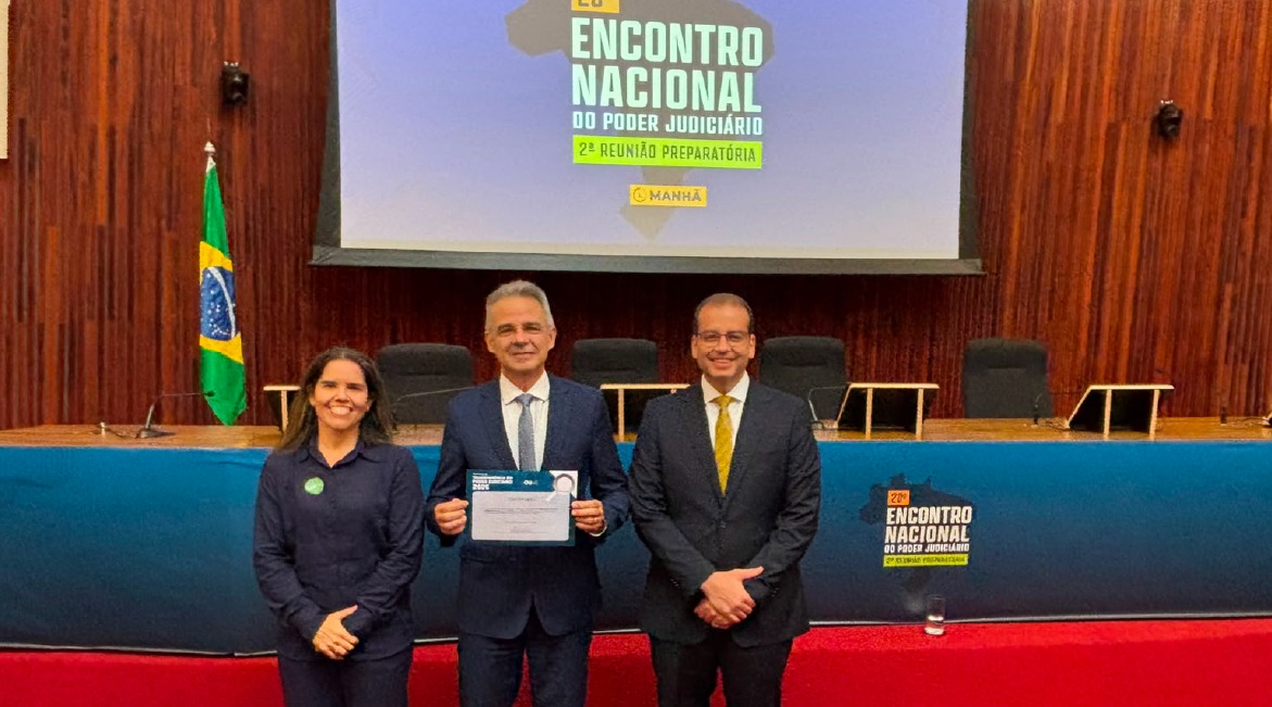 Imagem de dois homens e uma mulher, sorrindo para foto em pé, em um grande auditório