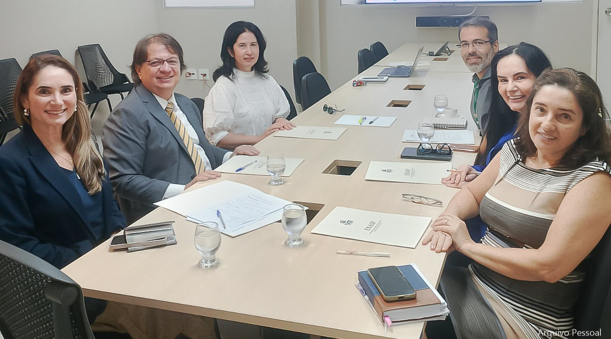 Pessoas sorridentes sentadas em uma mesa de reuniões posam para foto.
