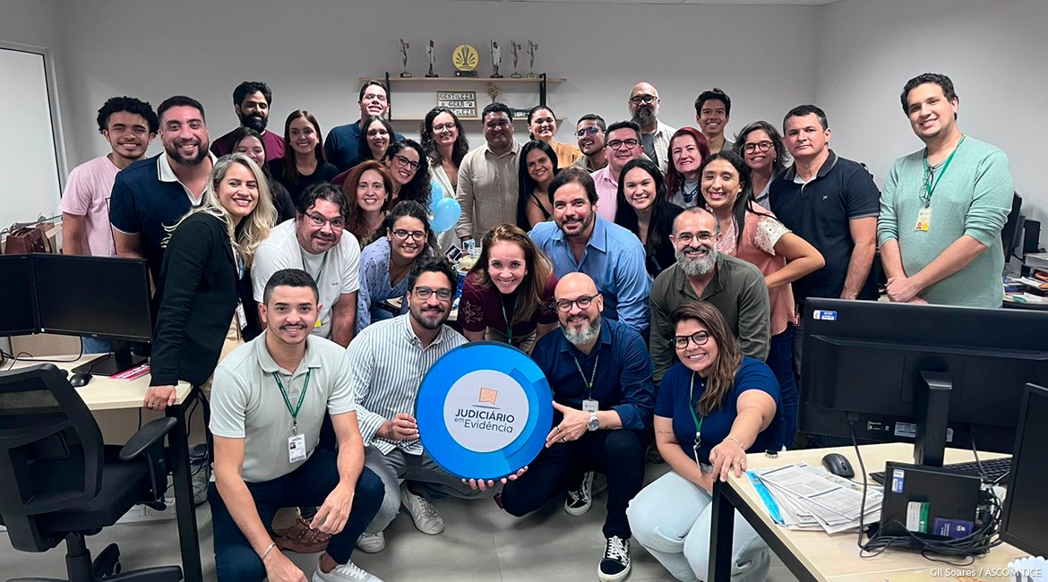 Imagem de várias pessoas em pé e agachadas posando para foto, sorrindo, em uma sala